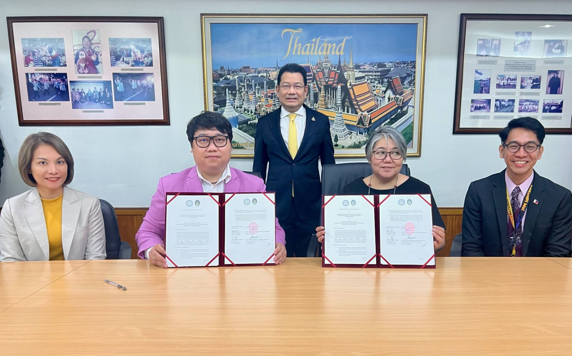 Representatives holding up signed agreement folders behind a conference table