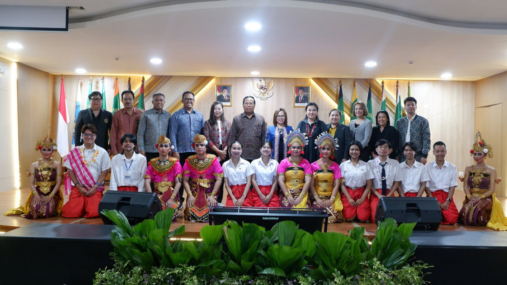 Students in traditional Indonesian dance attire kneeling before officials on a stage
