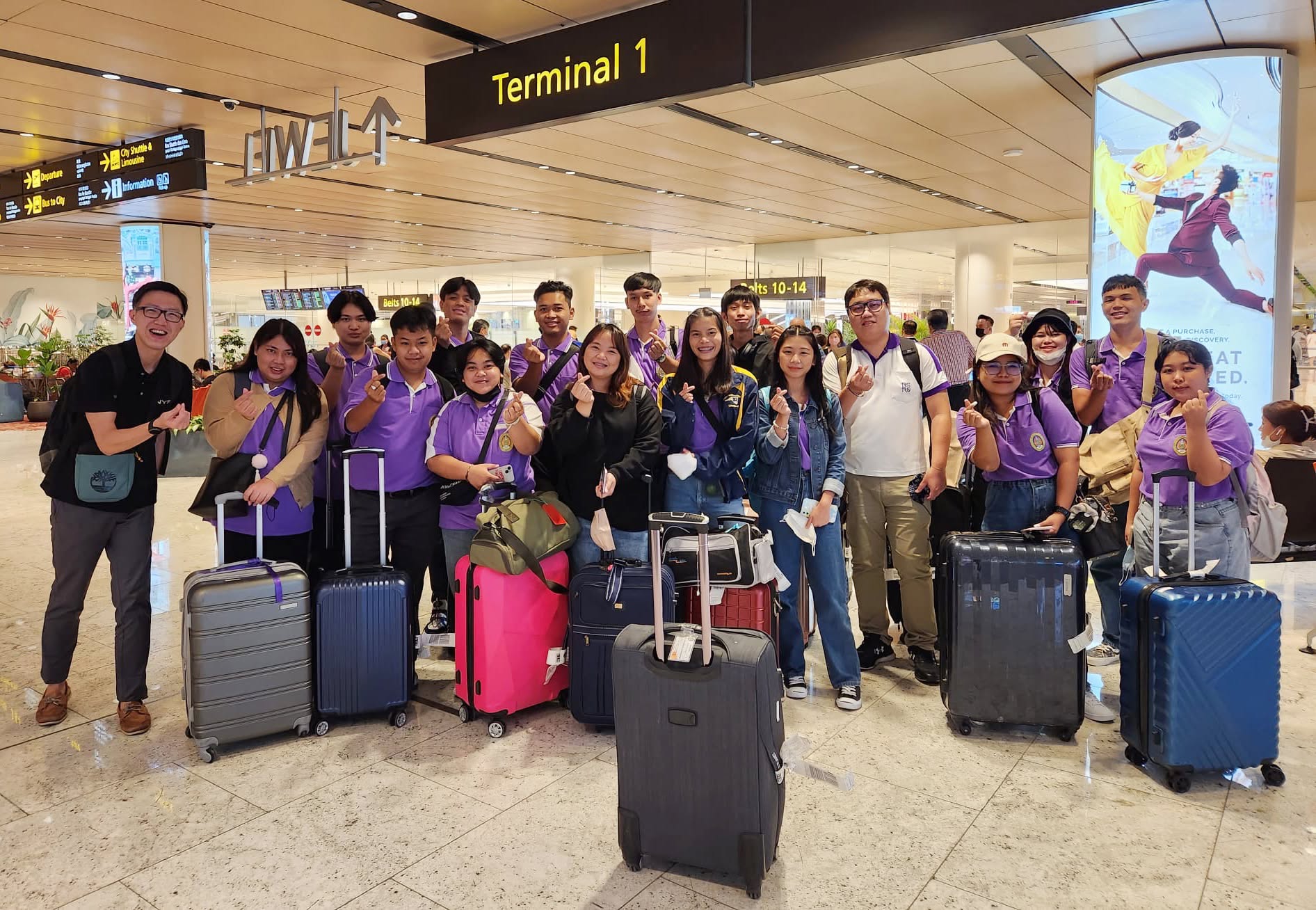 Students and staff in matching purple polo shirts posing with luggage in an airport terminal